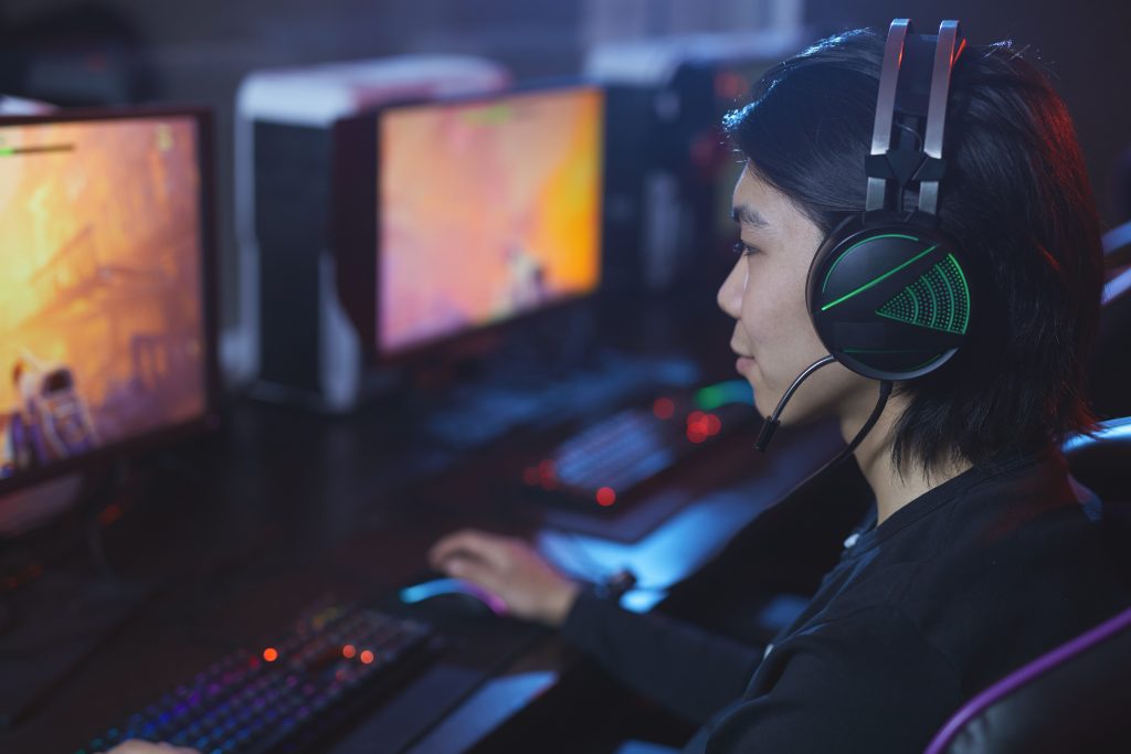 High angle portrait of young Asian man playing videogames and wearing headphones in dark cyber interior, copy space